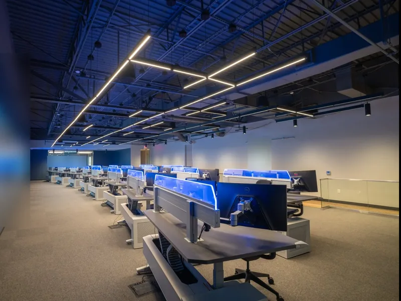 Operations floor of a GSOC built by Jim McDonald, operator consoles under a video wall
